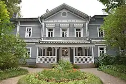 A blue two-story house with white trim and many windows, surrounded by birch trees.