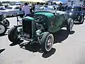 Hi-boy Deuce roadster with a flathead V8 (with factory head and exhaust but aftermarket alternator ignition and dual-carb intake), dropped tube axle, and drum brakes.