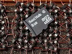 This microSDHC card holds 8 billion bytes (8 GB). It rests on a section of magnetic-core memory that uses 64 cores to hold eight bytes. The microSDHC card holds over one billion times more bytes in much less physical space.