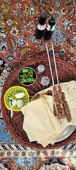 Skewered kebabs placed on a rectangular lavash, served as part of a meal.