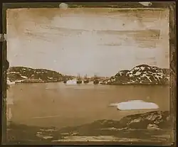 a sepia toned photographic view of four ships in the distance sailing through a channel.
