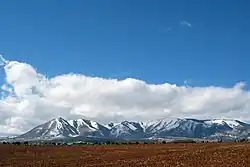 Snow-covered mountains protruding from a plain with tilled soil in the foreground.