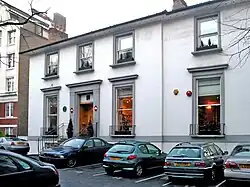 A two-storey white building with grey window frames, several cars parked in the foreground