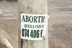 Torn flier on a pole reading: ABORTION / QUICK & PAIN FREE / 074 406 6 [rest of number illegible]