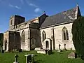 Stone building with square tower to left hand end. Foreground shows gravestones in grass area.