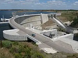 Alqueva dam with a road across its crest holds back a reservoir in a rural landscape.