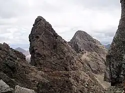 Rugged mountain scenery - several sharp prominences of bare grey rock stand out on a long ridge leading to more hills beyond.