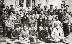 A large gathering of soldiers and several religious figures in dark robes and pointed hoods standing outside a grand stone cathedral.
