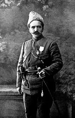 A black and white portrait photo of a man in a dark military coat with a large, thick mustache looking directly into the camera.