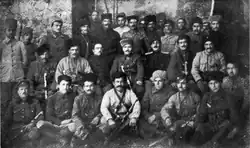 A black and white photo of a group of uniformed military officers standing in front of a rustic stone wall outdoors.