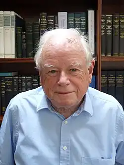 Photo of a man with white hair wearing a blue shirt.
