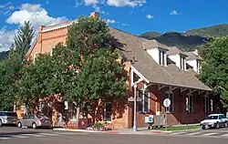 A brick building with trapezoidal roof overhanging the sidewalk on its right side at an intersection. Signs say it is at the 100 block of South Galena Street and the 500 block of East Hopkins Avenue.