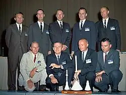 Official group portrait of the nExt Nine astronauts in front of models of the Mercury, Apollo, and Gemini spacecraft
