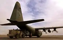 Rear view of a propeller-driven plane on the ground with its cargo door open and propellers still spinning