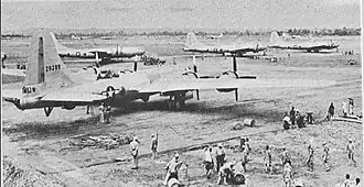 Four large 4-engined World War II–era aircraft sitting on the ground at an airstrip. Groups of people are working near each aircraft.