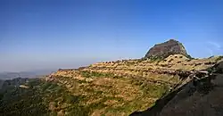 dark rocky hill surrounded by a small semi-desert plateau and deep cliffs