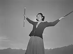 A black-and-white photography shows a smiling woman from below twirling batons with the sun behind her.