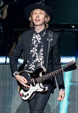 Beck onstage playing guitar and smiling, wearing a suit and hat