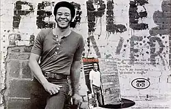 Withers smiling and leaning in front of a brick wall