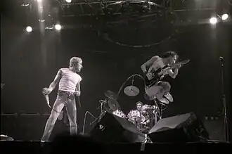 Roger Daltrey holding a microphone and Pete Townshend jumping on stage