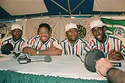 Four men seated behind microphones at a table, likely a music group