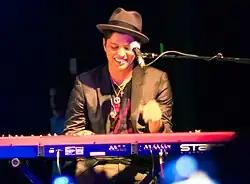 A smiling Mars onstage, seated at a keyboard