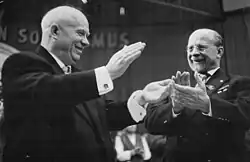 Two smiling men raise bouquets of flowers over their heads.