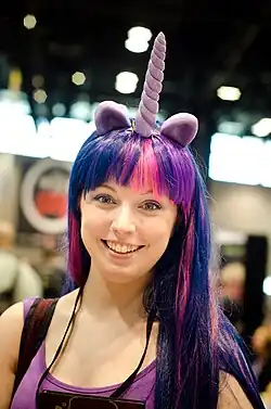 Smiling woman cosplaying Twilight Sparkle while wearing a purple and pink wig with light purple ears and a horn