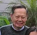 An old man, wearing a pullover is smiling.