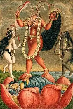 A decapitated, nude, red-complexioned goddess stands on a nuni inside a large lotus. She holds her severed head and a scimitar. Three streams of blood from her neck feed her head and two nude, red-coloured women holding a scimitar and a male severed head, who flank her. All three wear a garland of severed heads, a serpent (around her neck) and various gold and pearl jewellery.