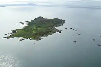 A green island sits in a calm sea. There are numerous small islets in the surrounding waters.