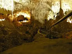 A picture of a partially illuminated cave with a jagged rock ceiling and a walkway extended into the cavern.