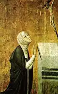 St. Catherine of Siena, wearing a white veil and black mantle, kneels in prayer before an altar with a crucifix.