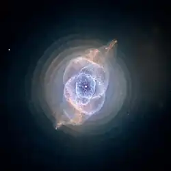 Blue-green diffuse disk with complex circular structure in its center. The disk is crossed by s-shaped brown curve