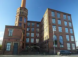 The same mill viewed from the front. It is now in good condition with new windows, none of which are boarded up. A sign above the gateway reads "Cavendish Mill"