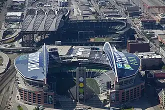 Two stadiums in an industrial area. Both have roofs with large arched trusses.