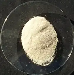 A small colorless saucer holding a pale-yellow powder