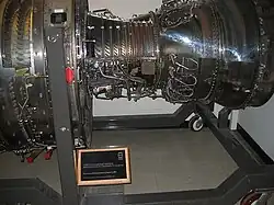 An engine public show at national museum, with the front aft facing left. Sections of the casing are trimmed out and replaced with clear plastic revealing booster vane, compressor and turbine blades, from left to right.