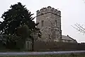 Square stone tower, behind a stone wall and partially obscured by a tree.