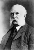 Portrait of an old man with a white beard. The man is wearing a jacket and a tie.
