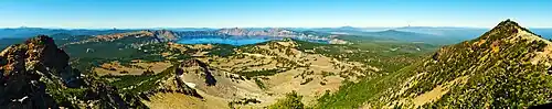 A panorama shot displays Crater Lake in the center background, with mountains in the foreground on the left and right