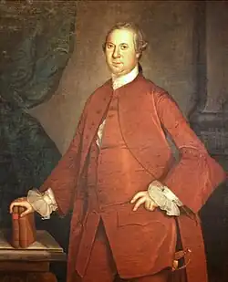 An eighteenth-century painting shows a middle aged man dressed in red clothing leaning on two books that are resting on a table, with a Roman-style column in the background