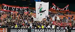 Fans wearing black cheer with several large graphics in a stadium's bleachers.
