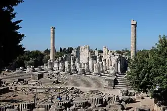 Color photograph, taken from the front, of the ruins of a Classical building, with white/grey columns and stairs.