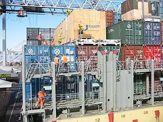 Dockworkers securing containers on a ship with steel lashing bars and turnbuckles