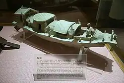 A pottery model of a boat with a steering rudder at the stern and a small sailor figurine standing on board
