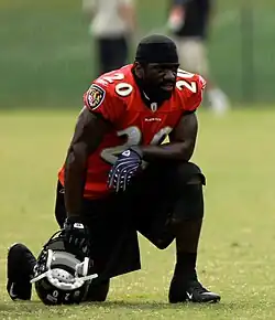 Ed Reed in a Baltimore Ravens jersey resting on one knee with his helmet on the ground in his hand.