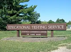 Large wooden sign with "Educational Testing Service" in white letters, on the law in front of ETS headquarters.
