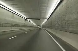 A two-lane freeway without any safety lanes or shoulders is proceeding down a lighted square passageway.