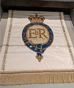 light-colored cloth banner with the initials E R II surrounded by the words 'Honi soit qui mal y pense' in a border, beneath a crown